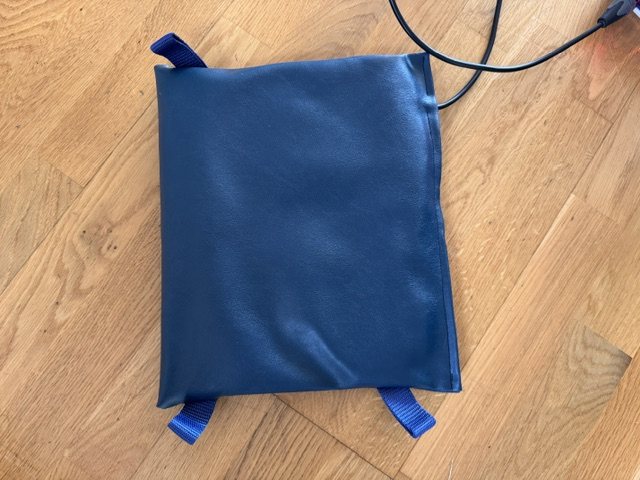 The therapy mat seen from above: a navy padded mat with blue webbing handles at its corners and the lead running from one side.